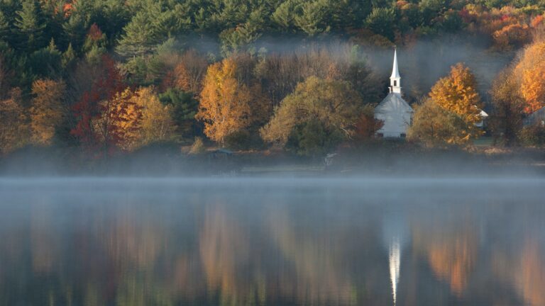 Colorful fall trees and a church across the water, something you might see in New Hampshire