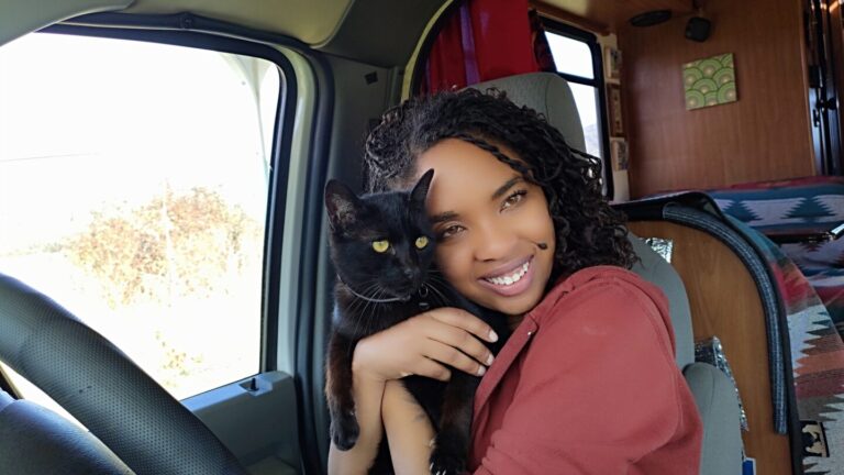 Young woman holds her cat seated at the wheel of her class c rv
