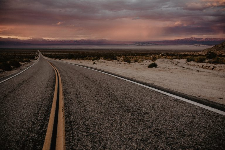 A two-lane highway cuts through flat prairie land under a purple sky.