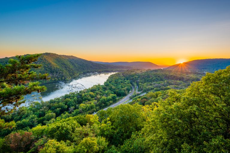 The sun rising over a valley, where a road travels parallel to a river.