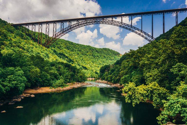 A long arched bridge spans high above a calm river with green trees on both sides.