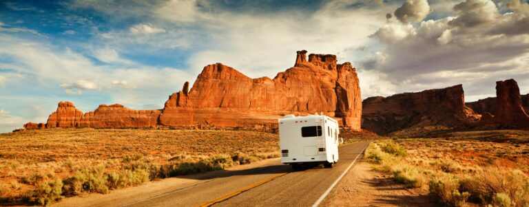 A Class C motorhome drives down a lonely road in Grand Canyon National Park with clouds overhead.