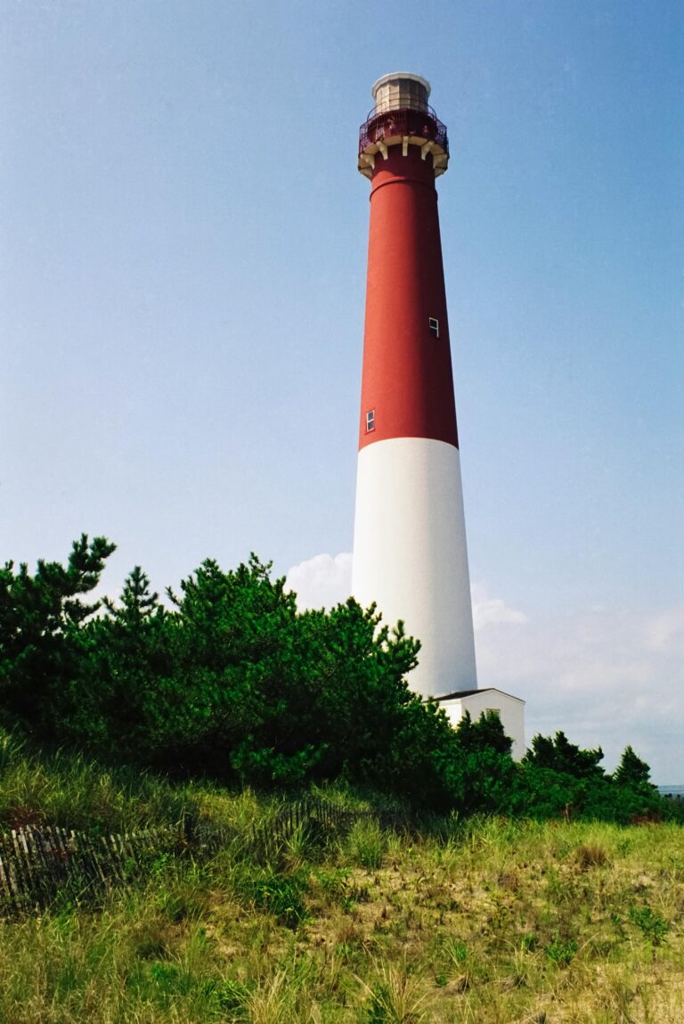 View of a red and white lighthouse from the dunes below