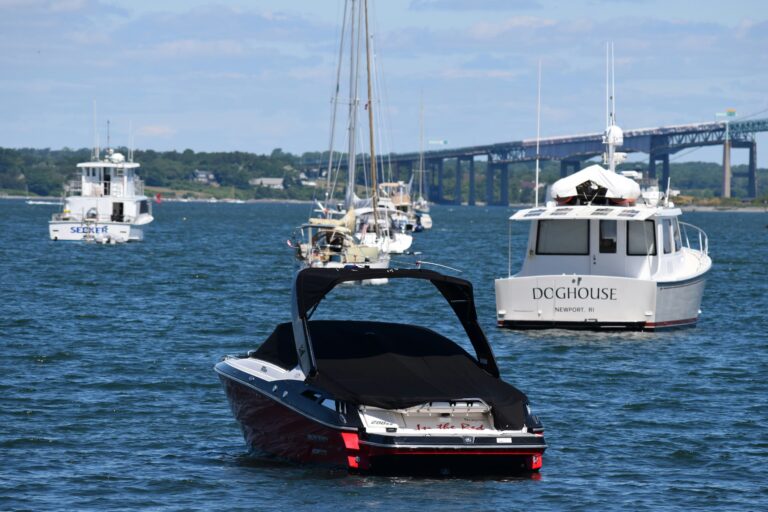 Several small boats sit in peaceful water next to a bridge and under sunlit skies.