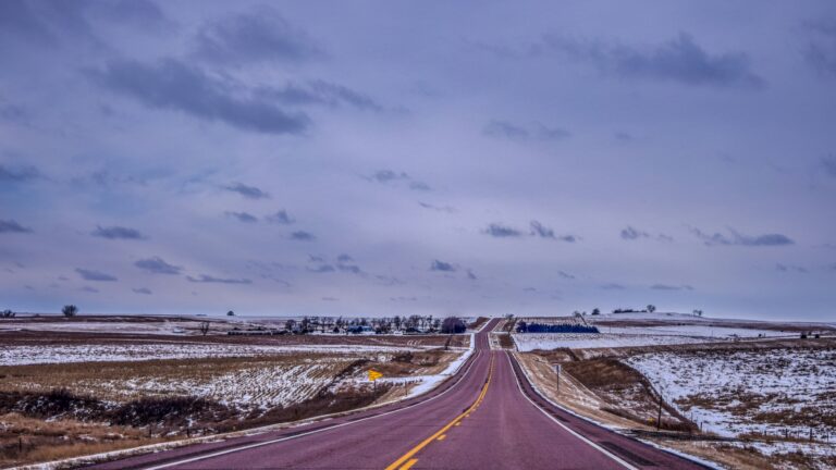 A highway with a yellow divider running through two snowy fields under an evening sky