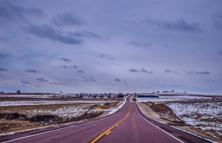 A highway with a yellow divider running through two snowy fields under an evening sky