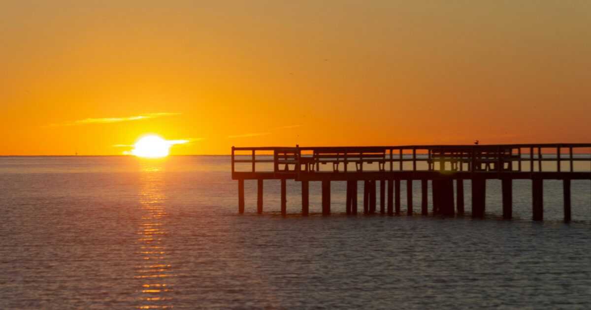 An orange sunset over vast waters with a large pier to the right