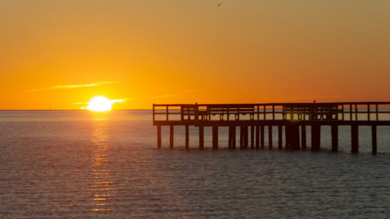 An orange sunset over vast waters with a large pier to the right