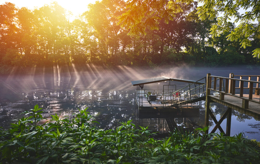 The rising sun burns away the fog over a river dock with seats for fishing in Arkansas
