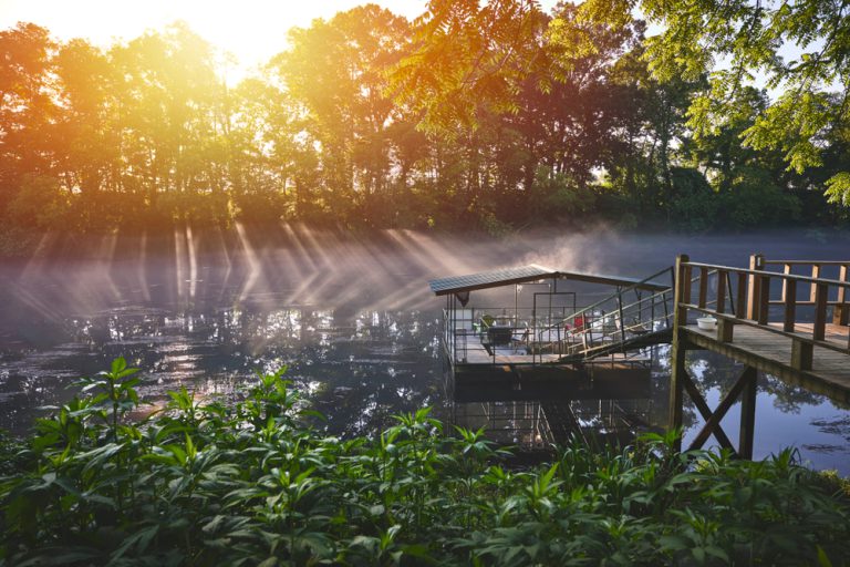 The rising sun burns away the fog over a river dock with seats.