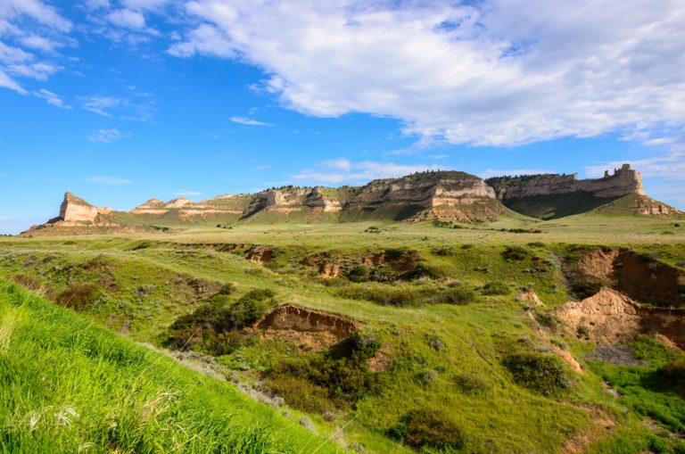 A hilly green plain leads towards unique bluffs in the distance.