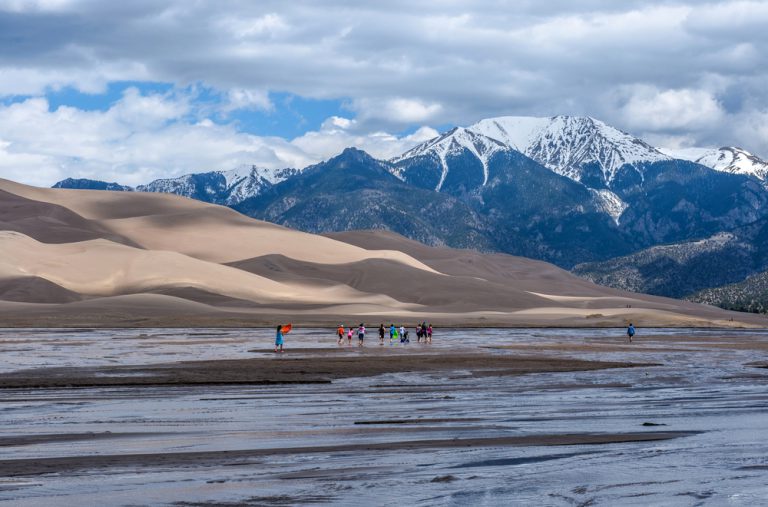 Great Sand Dunes National Park & Preserve, Colorado, USA - May 06, 2016: A group kids are playing in Medano Creek at the base of sand dunes and snow-capped peaks as spring clouds passing over.