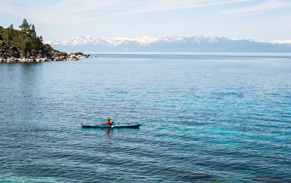 A person fishing in California from a kayak on a large blue lake.
