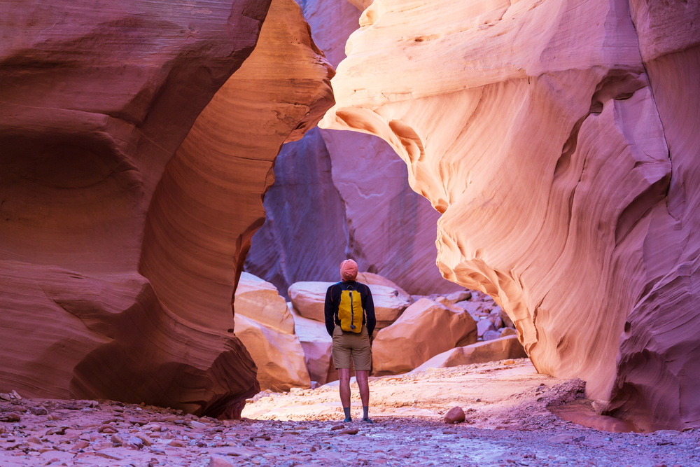 A hiker with a yellow backpack looks up at unusual rock formations in Grand Canyon National Park.