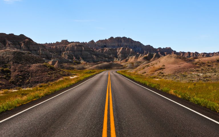 Looking down the center of a paved road in the middle of the Bad Hills, a hilly plain area.