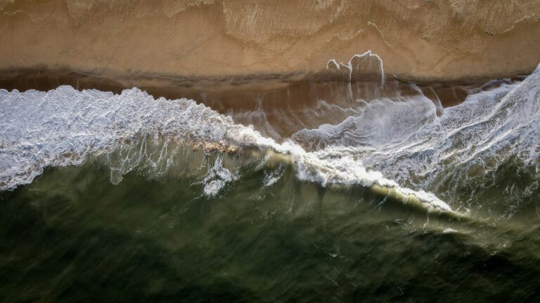 Overhead shot of waves crashing upon the sand of a beach on the Delaware coast