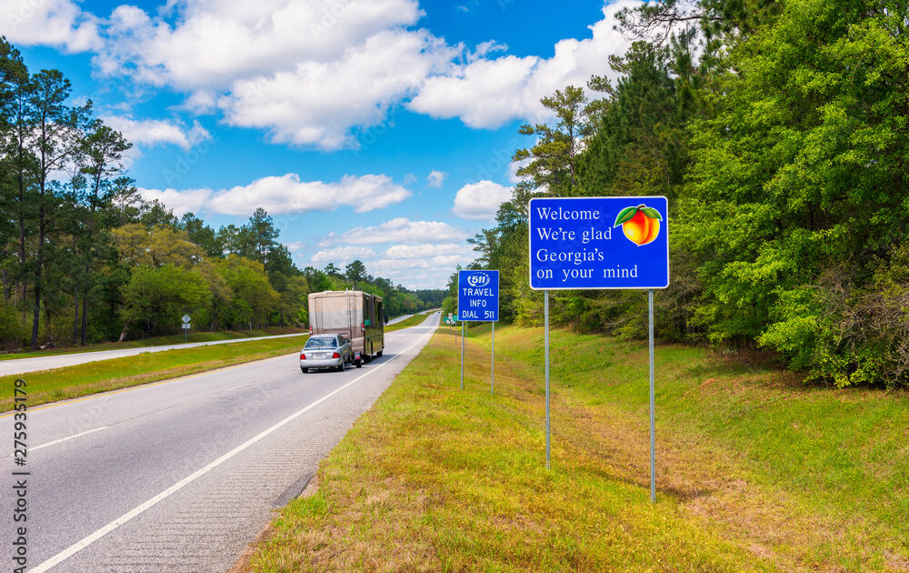A Class A motorhome pulling a car travels down the highway and passes a bright blue sign welcoming travelers to Georgia.