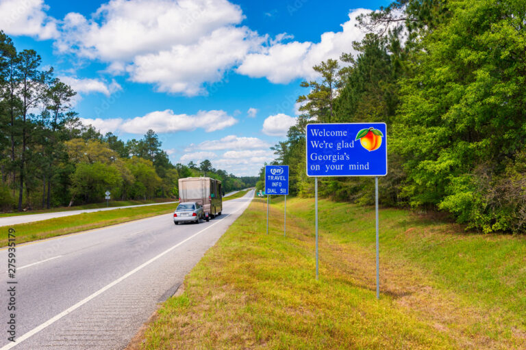 A Class A motorhome pulling a car travels down the highway and passes a bright blue sign welcoming travelers to Georgia.