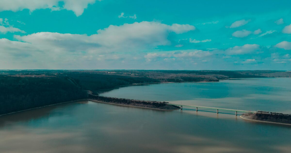 A wide body of water with a bridge running through it and a large area of blue and green land in the background