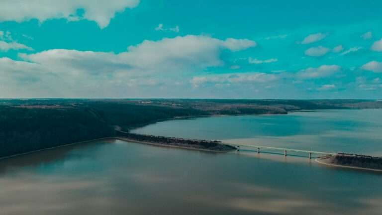 A wide body of water with a bridge running through it and a large area of blue and green land in the background