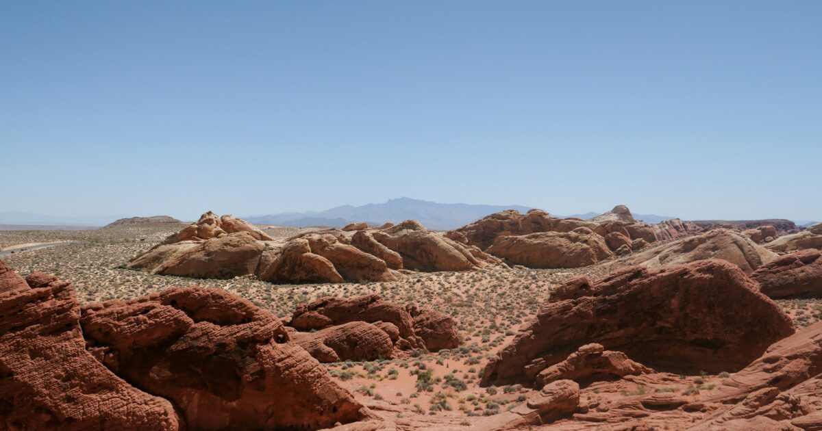 A stretch of desert landscape dotted with orange rock formations under a clear blue sky.