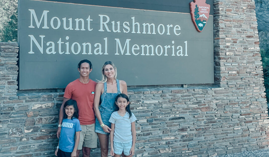 Family poses in front of Mount Rushmore National Memorial sign