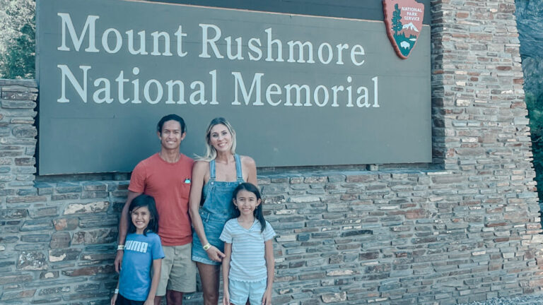 Family poses in front of Mount Rushmore National Memorial sign