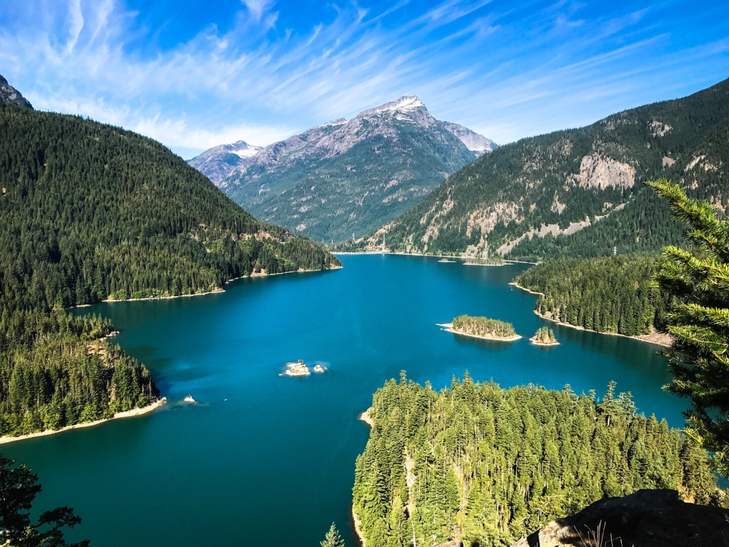 A bright blue lake sits between steep mountains covered with evergreen trees and rocky ridges - a serene spot for fishing in Washington