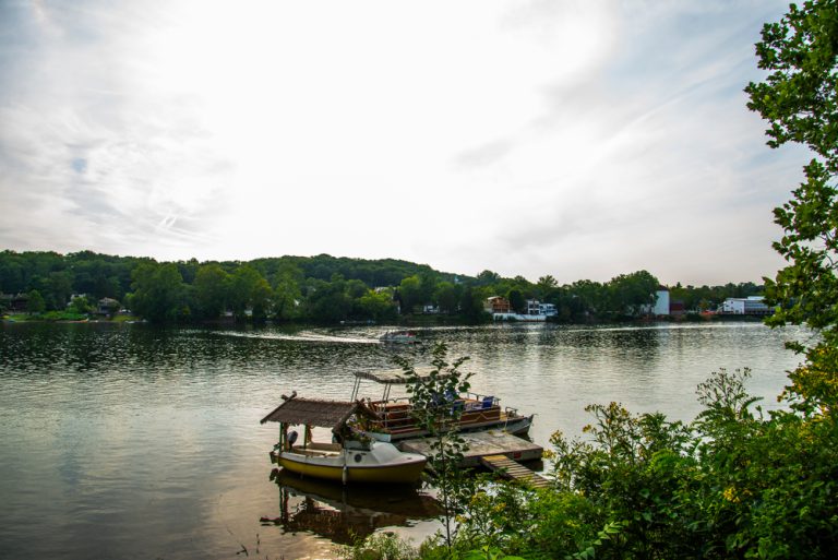 Two fishing boats docked at a sturdy wooden pier on the bank of a river. Other structures are seen on the opposite bank.