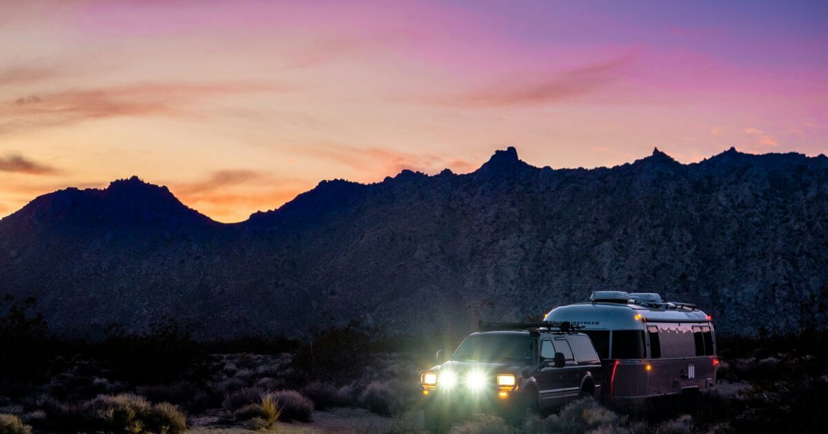 SUV and Airstream trailer camping beneath Arizona mountains at sunset under a dramatic pink sky.