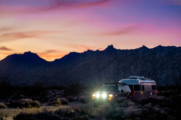 SUV and Airstream trailer camping beneath Arizona mountains at sunset under a dramatic pink sky.