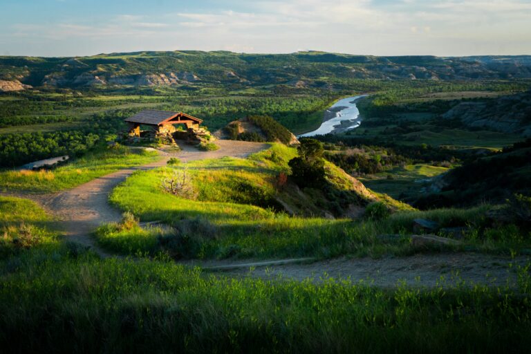 Log shelter overlooking winding river valley in Theodore Roosevelt National Park, with evening sunlight on green hills