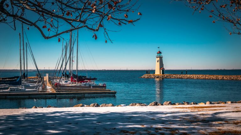 A shoreline next to a body of blue water, boats, and a lighthouse.