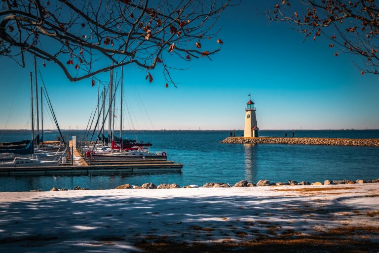 A shoreline next to a body of blue water, boats, and a lighthouse.