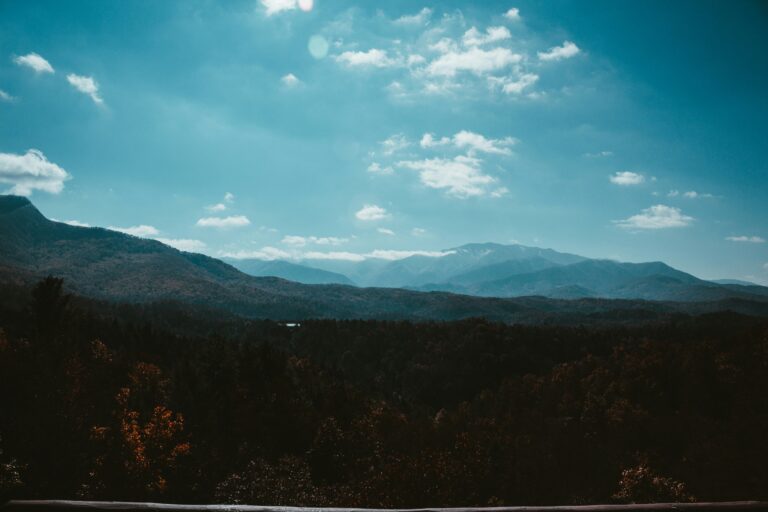 White clouds float through a blue sky over green mountains.