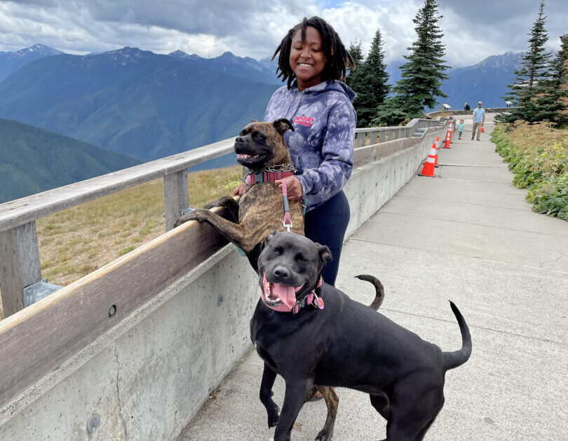 Woman smiles with her two dogs on an overlook