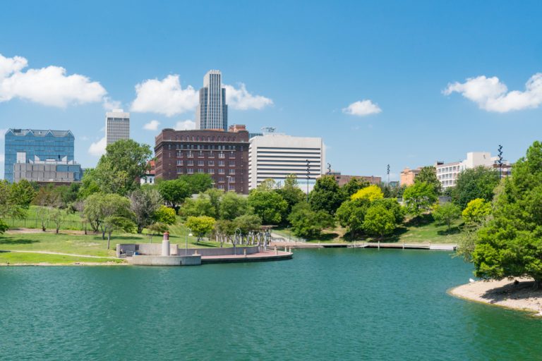 A cityscape peaks out from behind green trees across a blue lake.