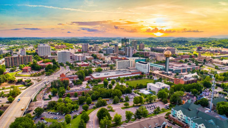 Aerial view of cityscape dotted with green trees under a setting sun.