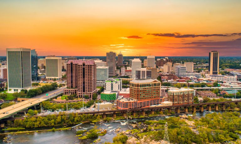 The sun sets over a city lined with a road and a canal boardwalk.