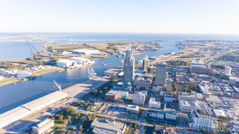 High-rise buildings sitting beside a river emptying into a vast blue ocean under a sunny sky