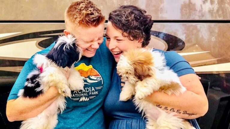 Couple holds their two shih tzus standing in front of their RV.