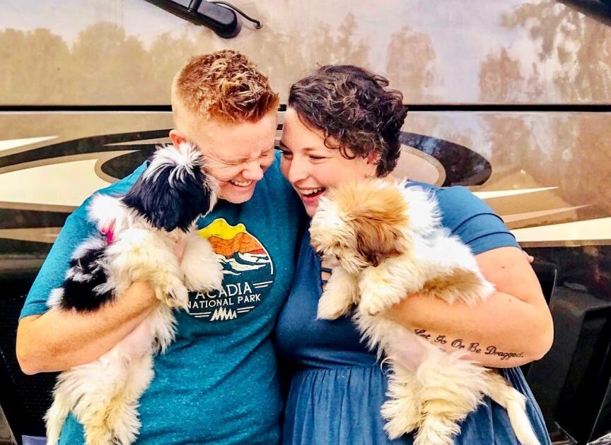 Couple holds their two shih tzus standing in front of their RV.