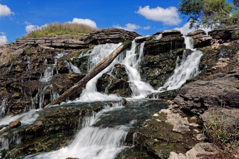 The water rushes over the Lake MacBride Waterfall. This waterfall has several main falls and numerous smaller falls.