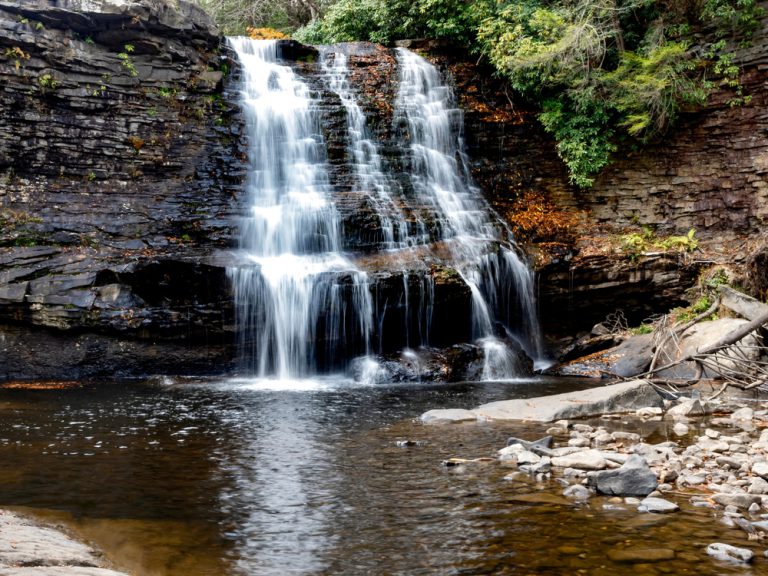 Muddy Falls in Swallow Falls State Park in Oakland, Maryland, the waterfall cascading and flowing down the side of the rocks in the autumn with leaves fallen in the water below.