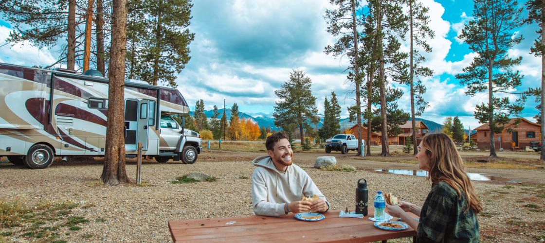 couple sitting at a picnic table with RV in the distance