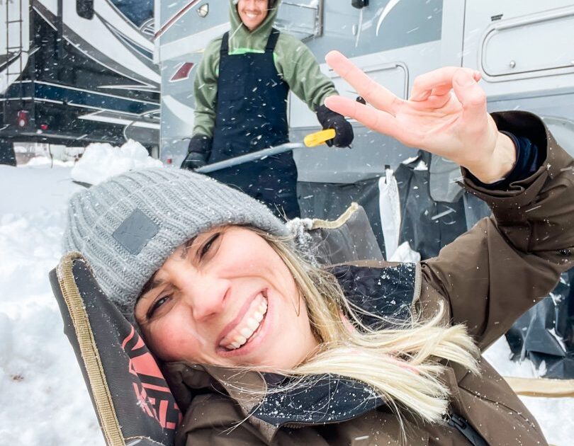 woman smiling in front of an RV on a snowy day