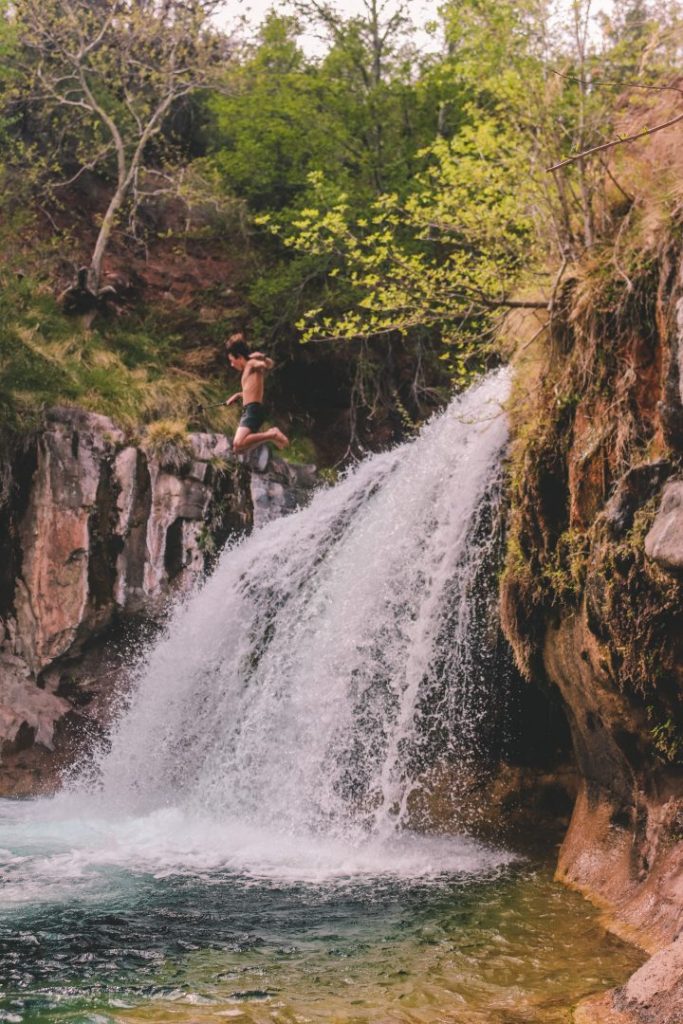 person jumps off waterfall into lake