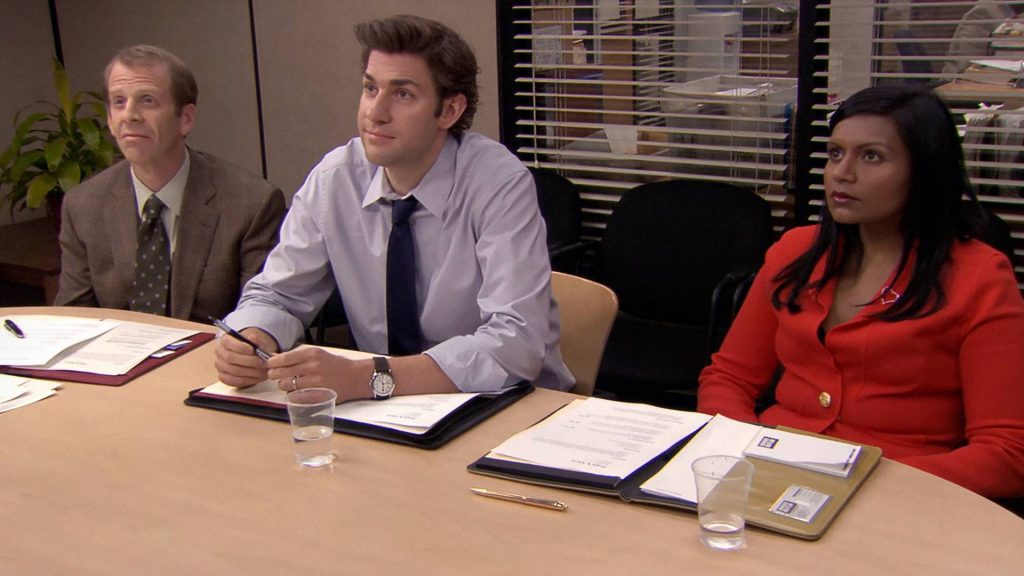 Kelly, Jim, and Toby sit the conference table of The Office show