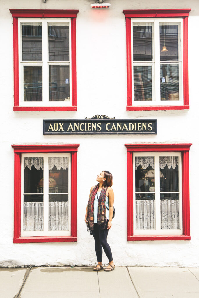 Woman stands outside of a building in Quebec City under a sign that reads "aux anciens canadiens"