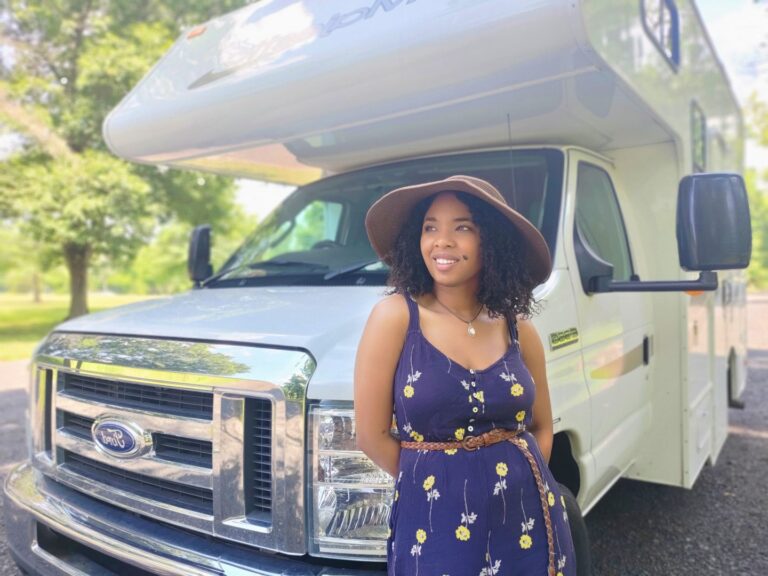 Young woman leans against the front of her Class C RV